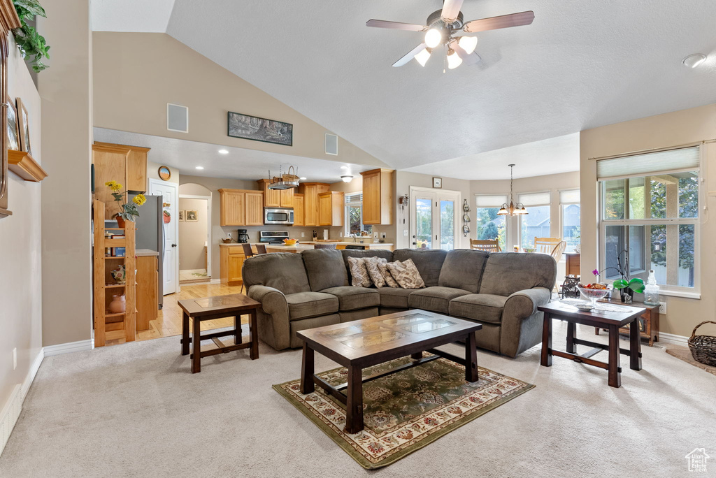 Carpeted living room with high vaulted ceiling and ceiling fan with notable chandelier