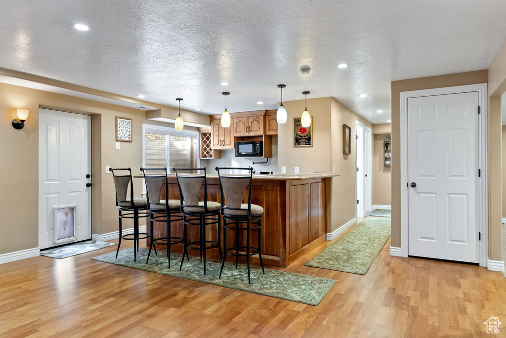 Kitchen with a textured ceiling, a kitchen breakfast bar, decorative light fixtures, and light wood-type flooring