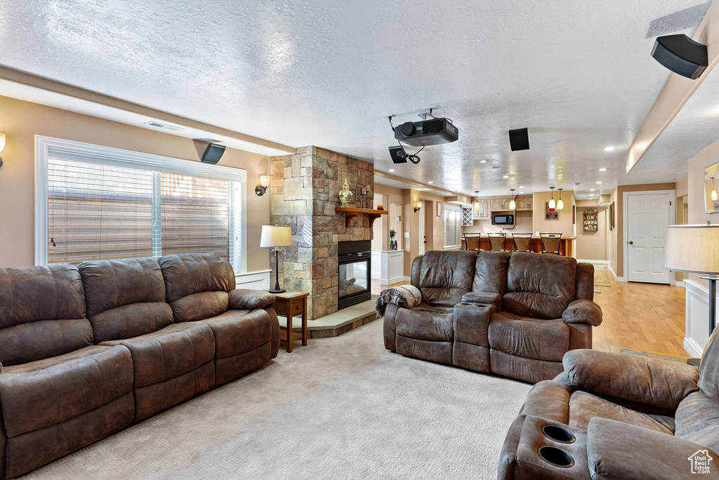 Living room with a textured ceiling, light colored carpet, and a stone fireplace