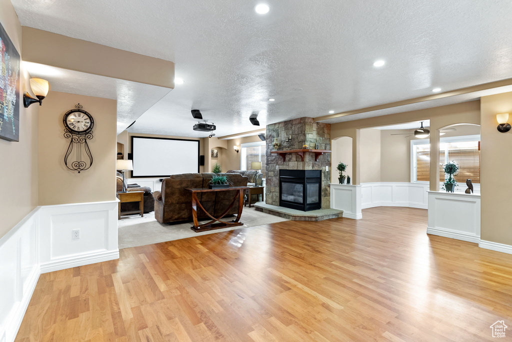 Living room with a stone fireplace, ceiling fan, light hardwood / wood-style flooring, and a textured ceiling