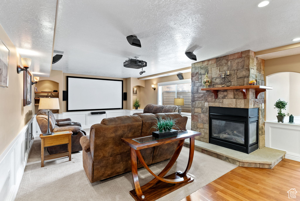 Cinema with light hardwood / wood-style floors, a stone fireplace, and a textured ceiling