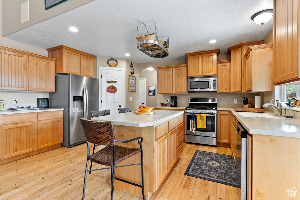 Kitchen with appliances with stainless steel finishes, light hardwood / wood-style flooring, a kitchen island, and sink