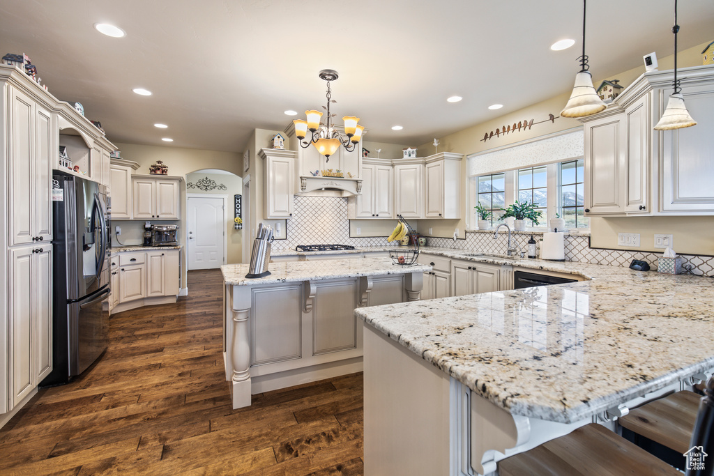 Kitchen featuring dark wood-type flooring, hanging light fixtures, a breakfast bar, a kitchen island, and appliances with stainless steel finishes