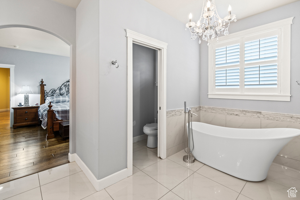 Bathroom with a bathing tub, an inviting chandelier, toilet, tile walls, and hardwood / wood-style flooring