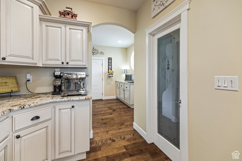 Kitchen with white cabinets, dark hardwood / wood-style floors, and light stone countertops