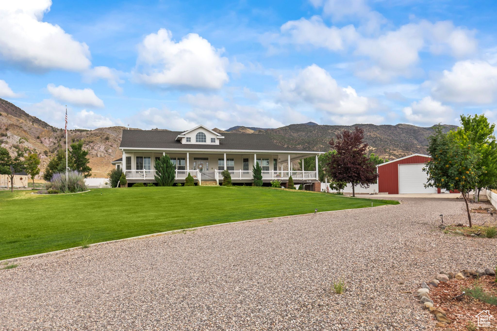 Farmhouse inspired home featuring a mountain view, an outdoor structure, gravel driveway, a porch, and a front yard