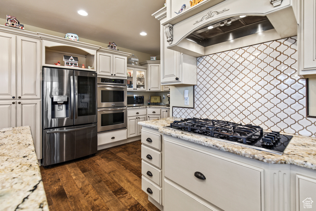 Kitchen with light stone countertops, dark wood-type flooring, stainless steel appliances, range hood, and white cabinets