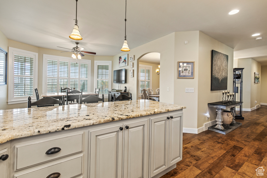 Kitchen with white cabinets, dark hardwood / wood-style floors, ceiling fan, light stone countertops, and decorative light fixtures