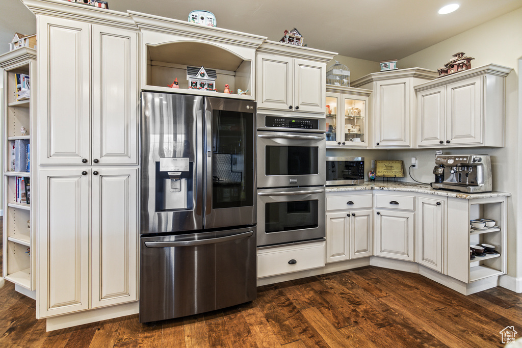 Kitchen featuring white cabinets, appliances with stainless steel finishes, dark hardwood / wood-style floors, and light stone counters