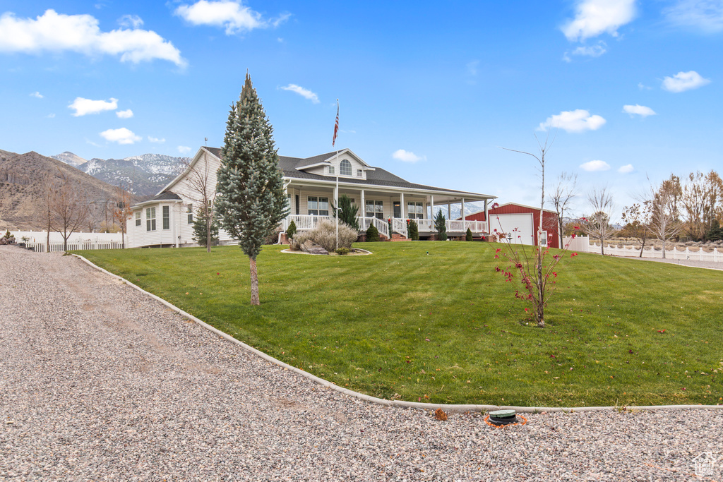 Farmhouse-style home featuring a front lawn, an outbuilding, a mountain view, covered porch, and a garage