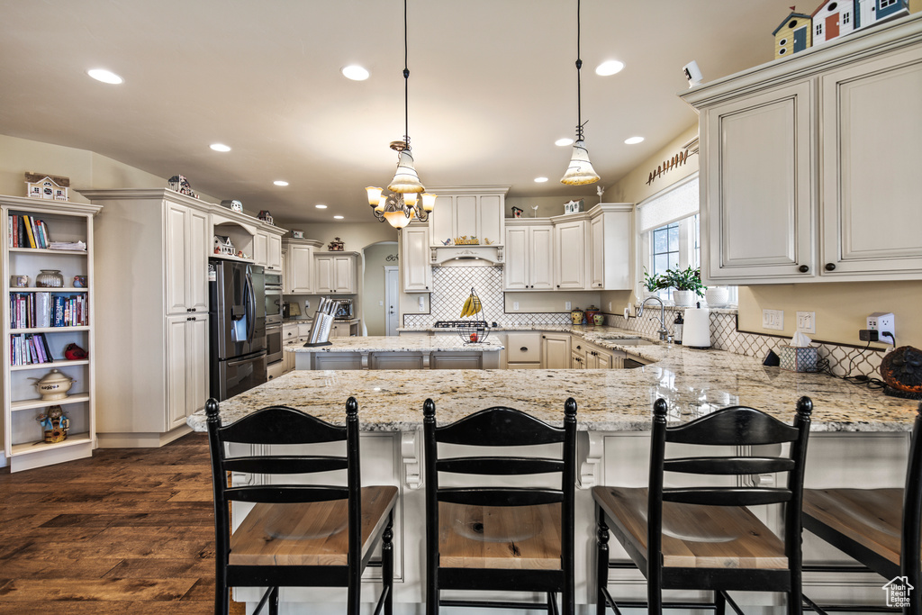 Kitchen with a breakfast bar, dark wood-type flooring, sink, decorative light fixtures, and stainless steel fridge with ice dispenser