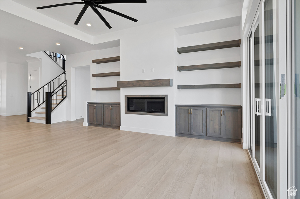 Unfurnished living room with stairway, light wood-type flooring, a ceiling fan, a glass covered fireplace, and recessed lighting