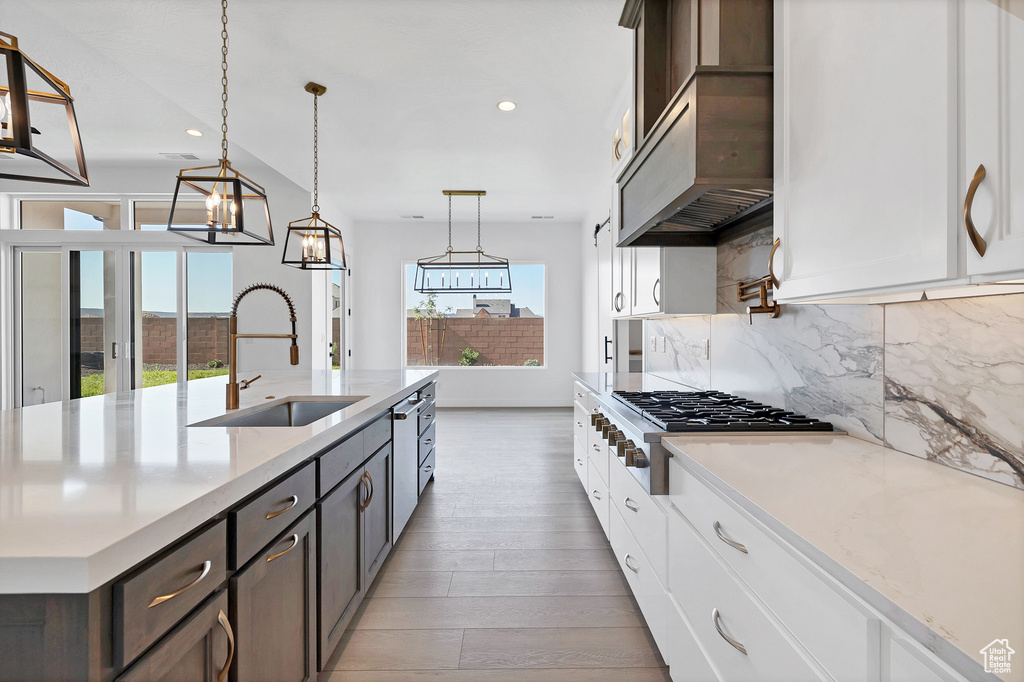 Kitchen with decorative backsplash, stainless steel gas stovetop, light wood-style floors, recessed lighting, and white cabinetry