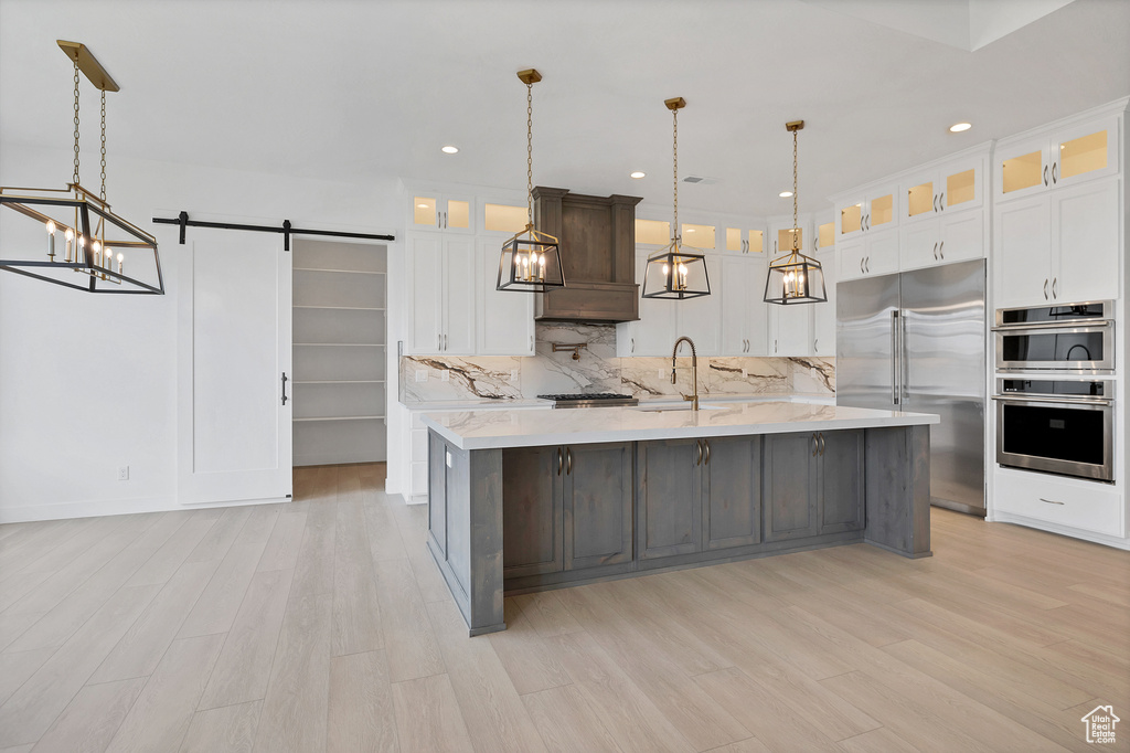 Kitchen with stainless steel appliances, a chandelier, backsplash, a barn door, and light wood-style flooring