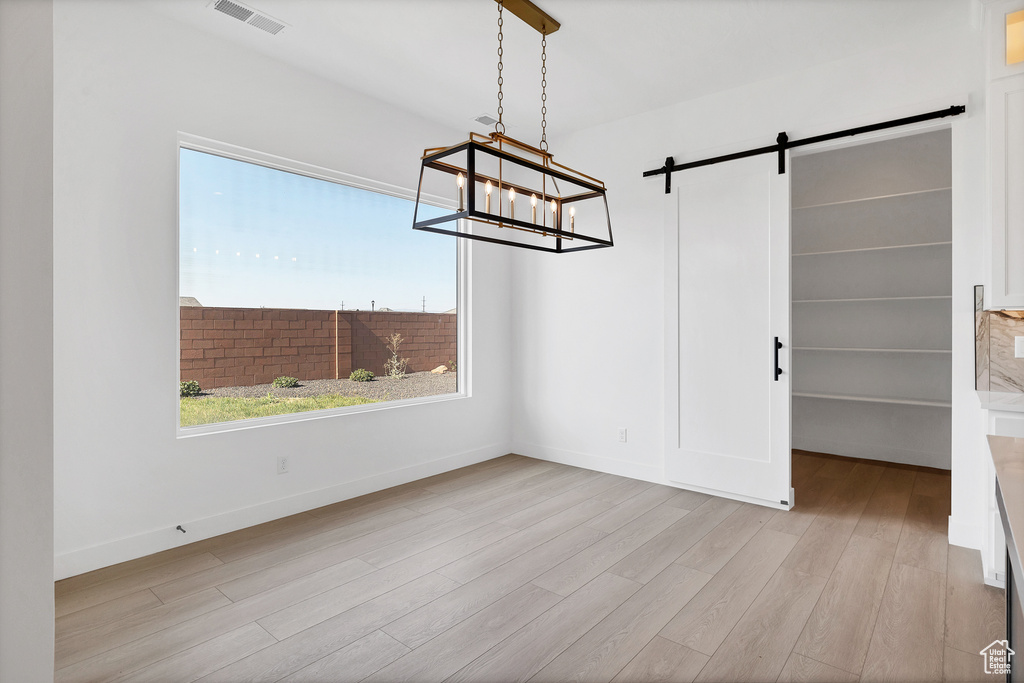 Unfurnished dining area with wood finished floors, plenty of natural light, a barn door, and a chandelier