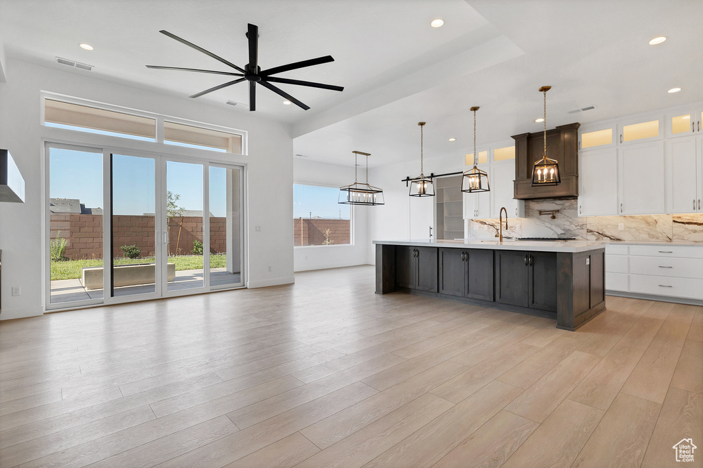 Kitchen featuring light countertops, a chandelier, open floor plan, a ceiling fan, and an island with sink