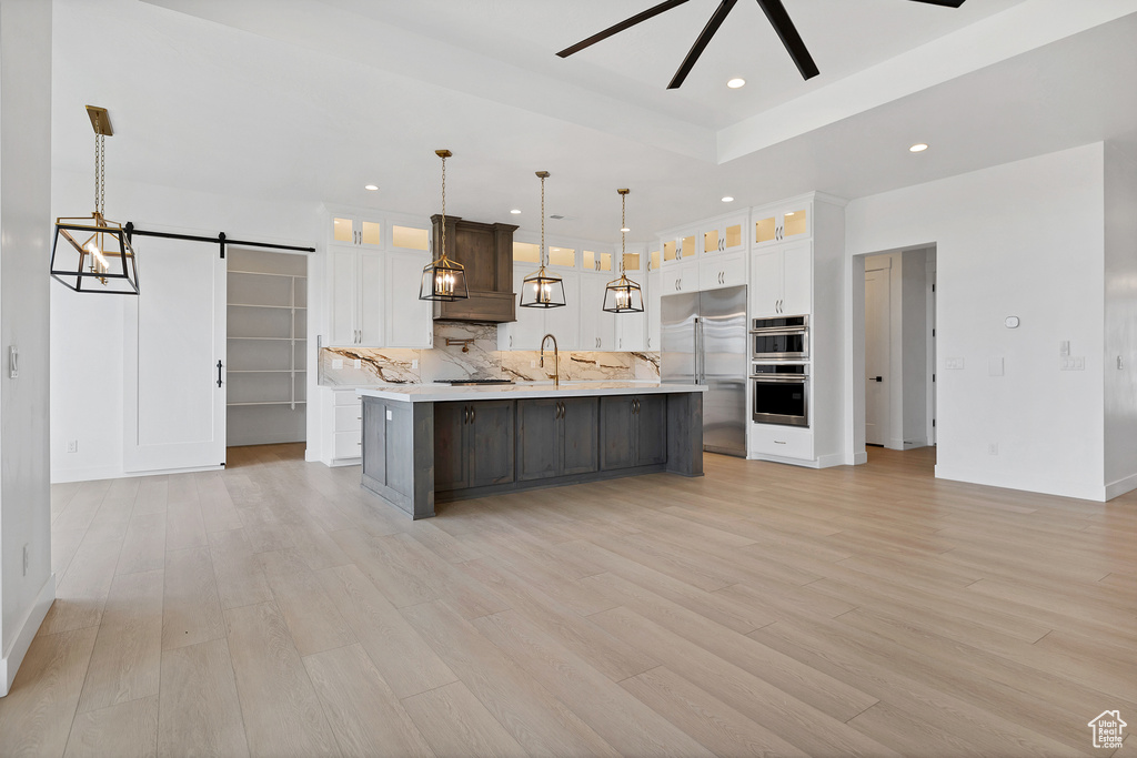 Kitchen with appliances with stainless steel finishes, light countertops, a barn door, a spacious island, and white cabinetry