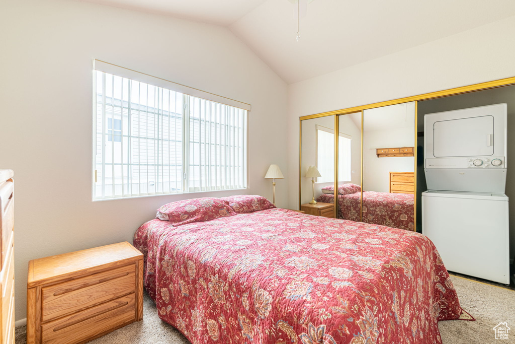 Carpeted bedroom with a closet, lofted ceiling, and stacked washer / dryer