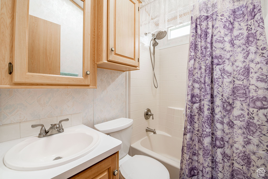Bathroom featuring shower / bathtub combination with curtain, wallpapered walls, toilet, and vanity