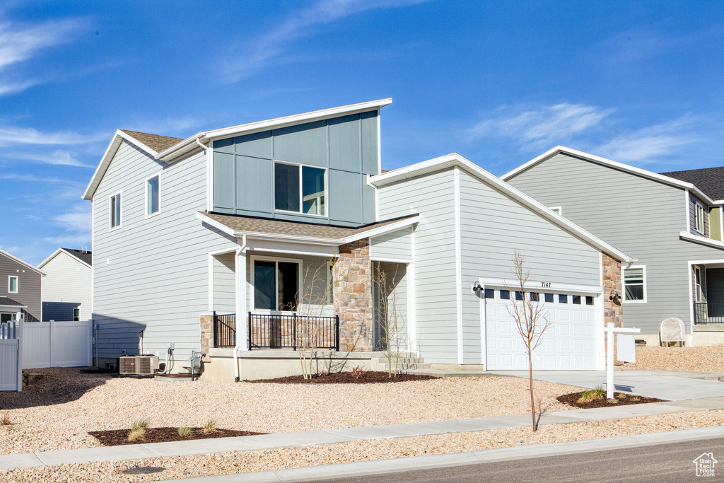 Modern home with covered porch, driveway, central air condition unit, stone siding, and a garage