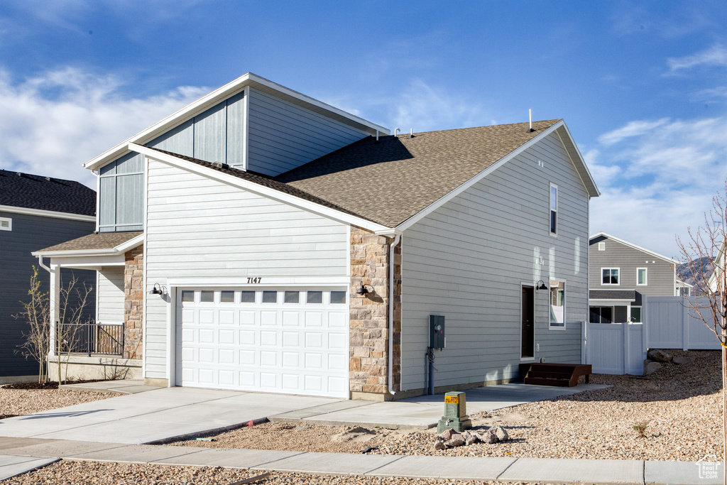 View of side of home with a shingled roof, stone siding, driveway, and fence