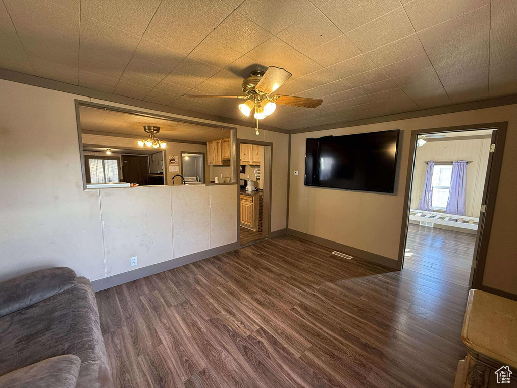 Unfurnished living room with ceiling fan, crown molding, and dark wood-type flooring