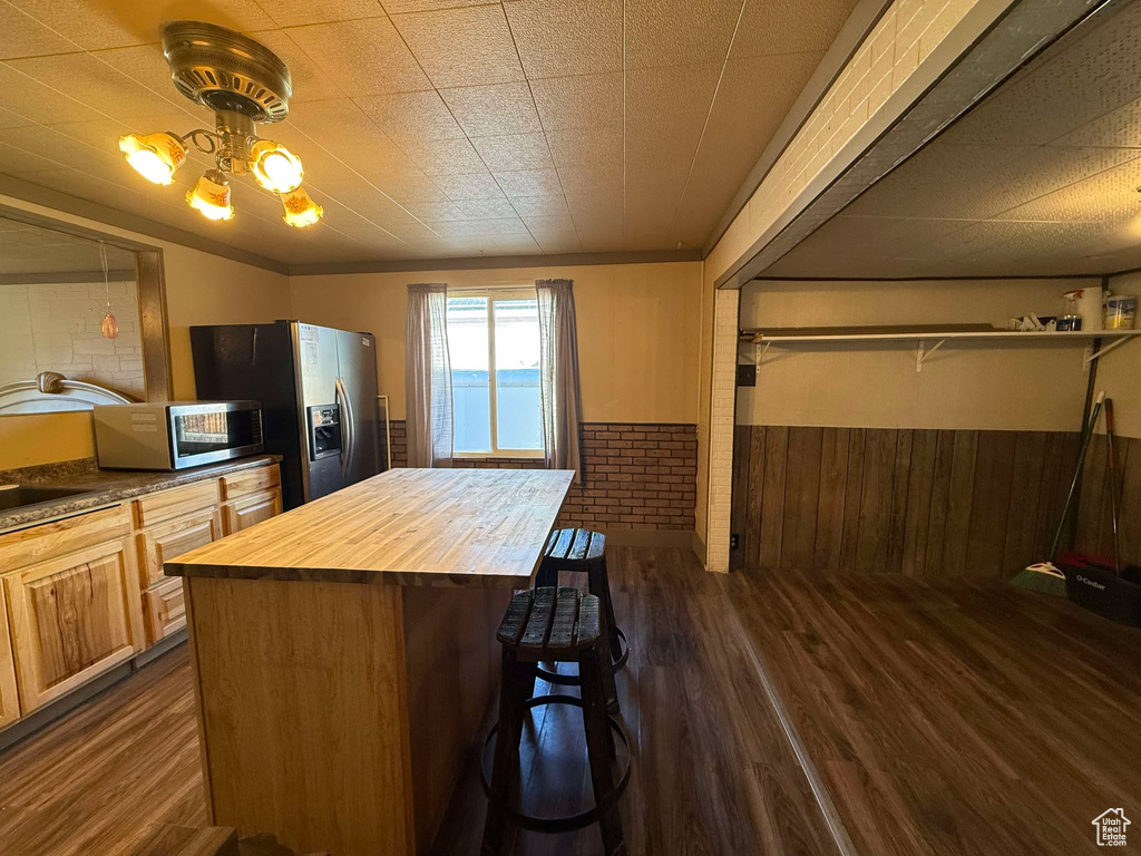 Kitchen featuring a breakfast bar, butcher block counters, stainless steel appliances, dark hardwood / wood-style floors, and brick wall