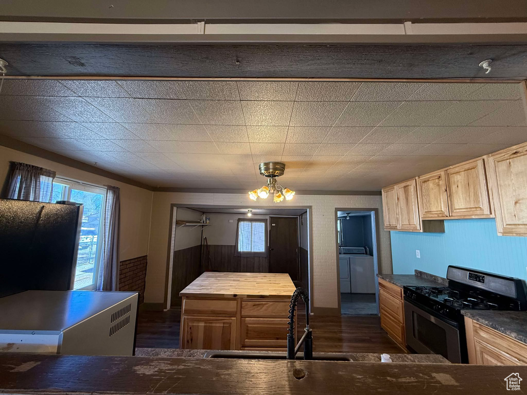 Kitchen featuring sink, stainless steel gas range oven, light brown cabinets, dark hardwood / wood-style floors, and washer and clothes dryer