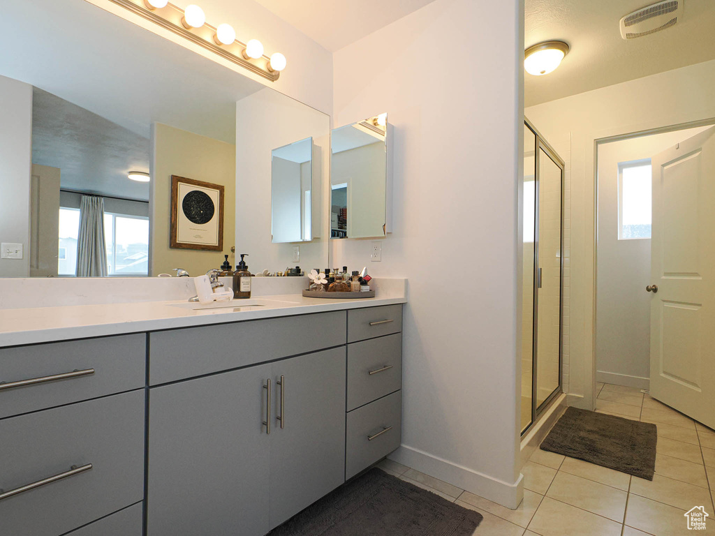 Bathroom featuring vanity, tile patterned floors, a wealth of natural light, and a shower with shower door