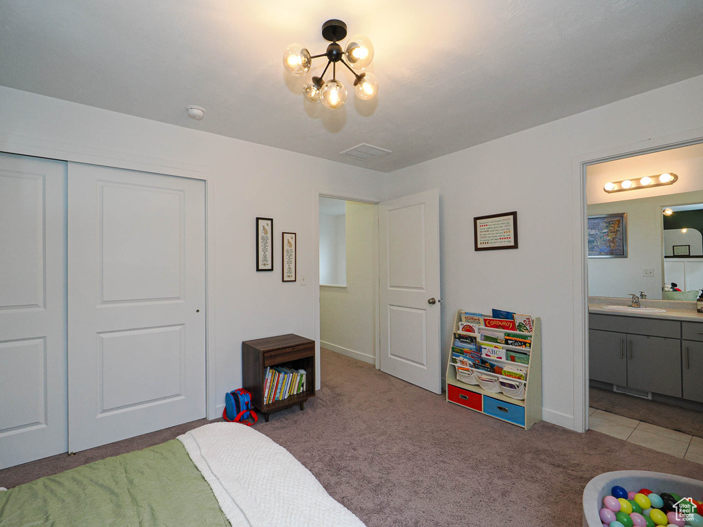 Carpeted bedroom with an inviting chandelier, sink, connected bathroom, and a closet