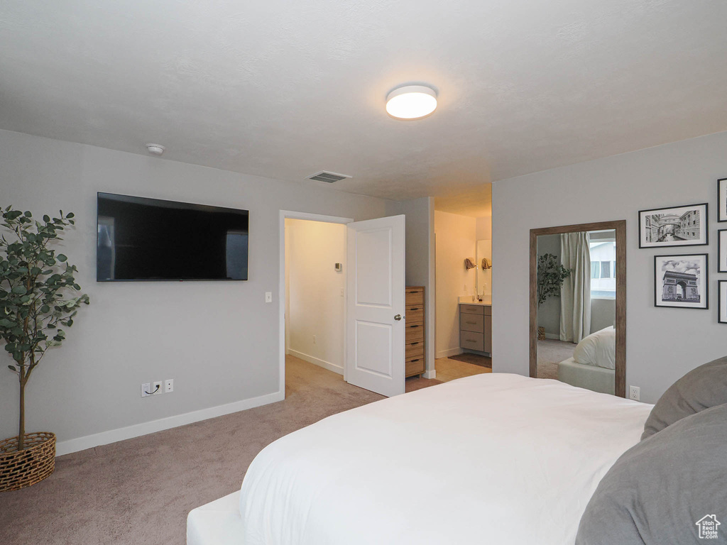 Bedroom with connected bathroom and light colored carpet