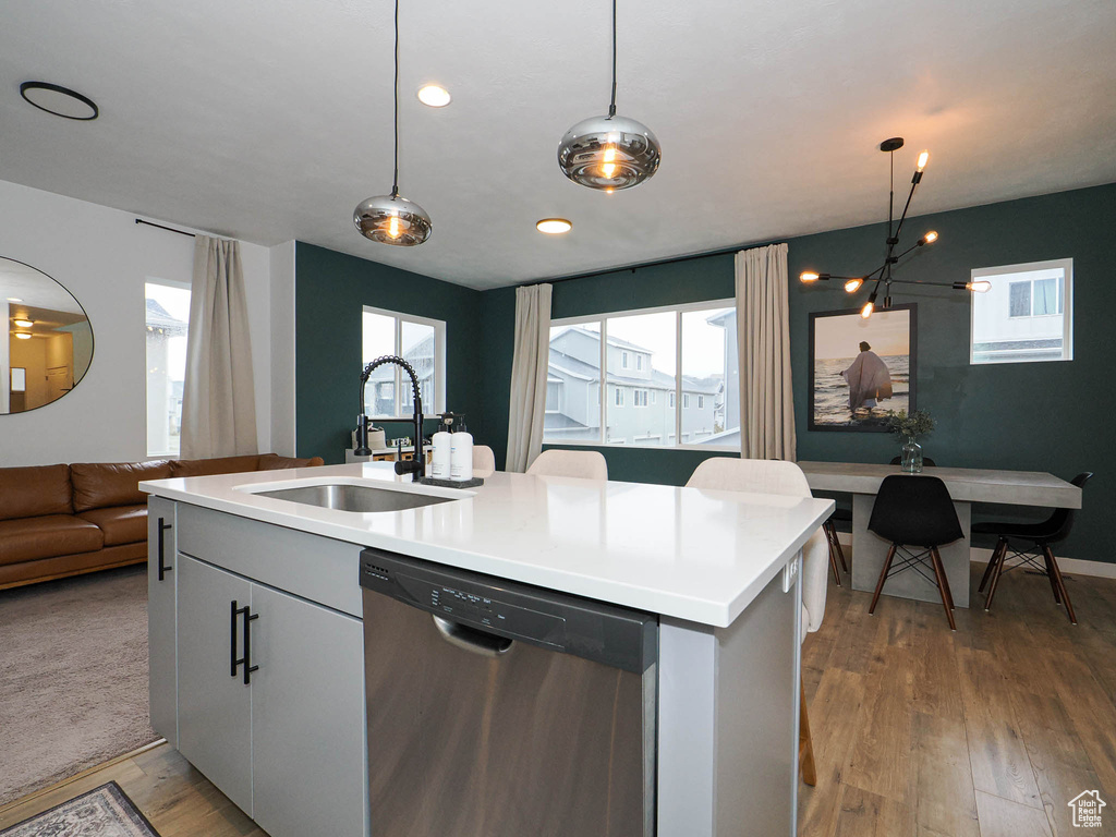 Kitchen featuring sink, stainless steel dishwasher, hanging light fixtures, and a kitchen island with sink