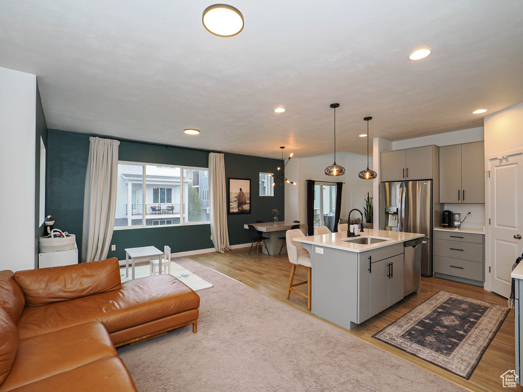 Kitchen featuring gray cabinets, an island with sink, pendant lighting, and light wood-type flooring