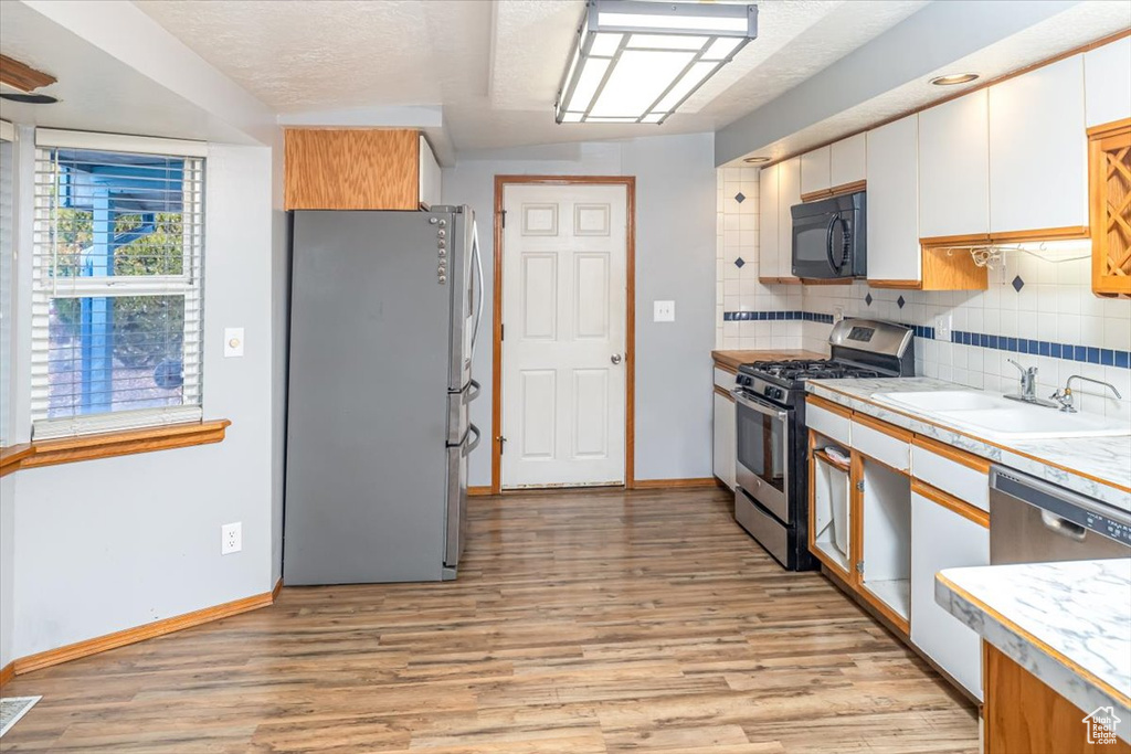 Kitchen with decorative backsplash, light wood-type flooring, white cabinetry, and stainless steel appliances