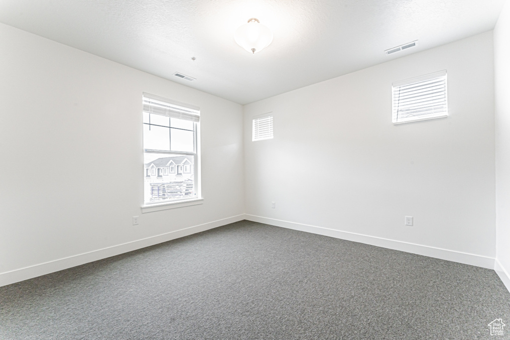 Unfurnished room featuring healthy amount of natural light, baseboards, and dark colored carpet