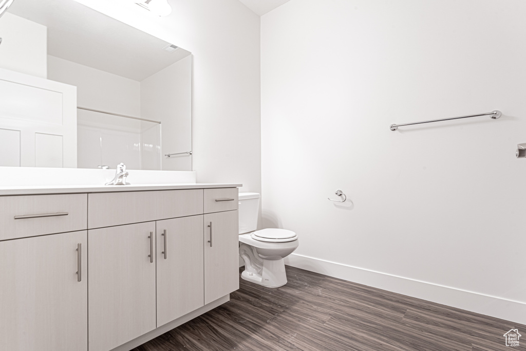 Full bath featuring vanity, toilet, baseboards, wood finished floors, and a shower
