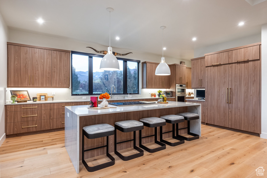 Kitchen featuring decorative light fixtures, light wood-type flooring, double oven, a large island, and a kitchen bar