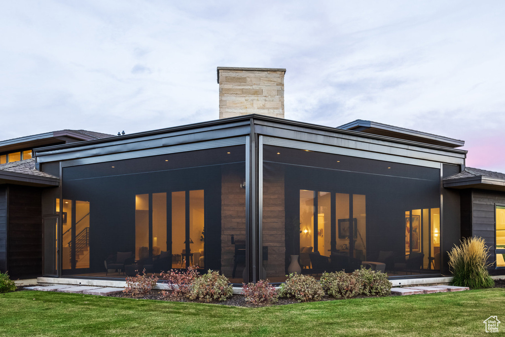 Back house at dusk with a yard and a sunroom