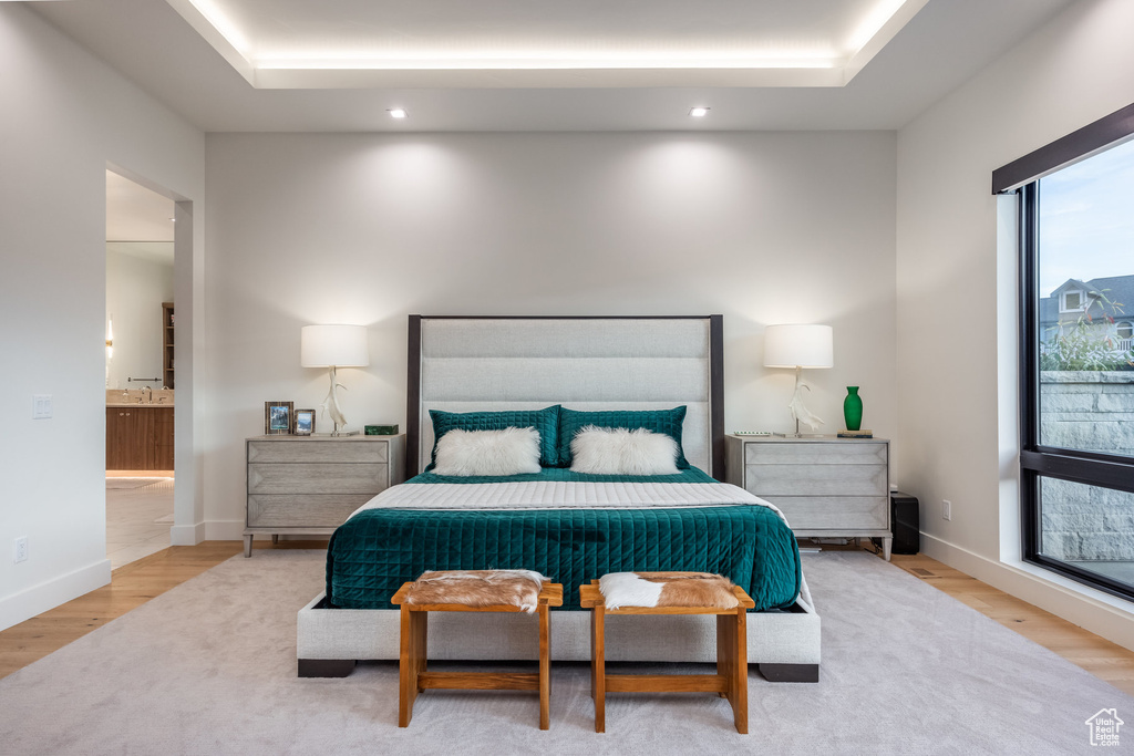 Bedroom with a raised ceiling, connected bathroom, and light hardwood / wood-style flooring