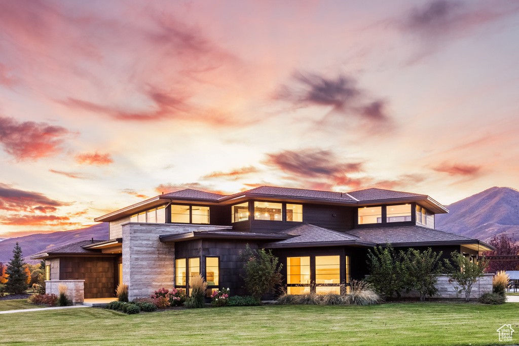 Back house at dusk with a mountain view and a lawn