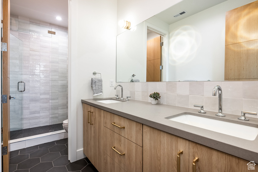 Bathroom with a tile shower, tile patterned flooring, toilet, decorative backsplash, and vanity