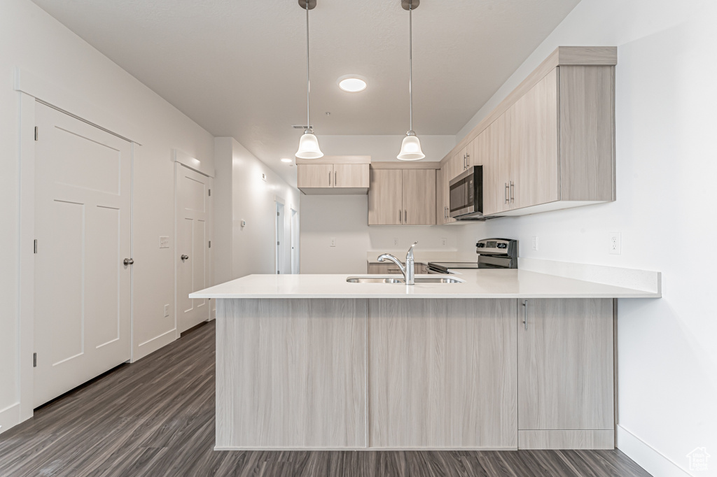 Kitchen featuring stainless steel appliances, a sink, a peninsula, light countertops, and light brown cabinetry