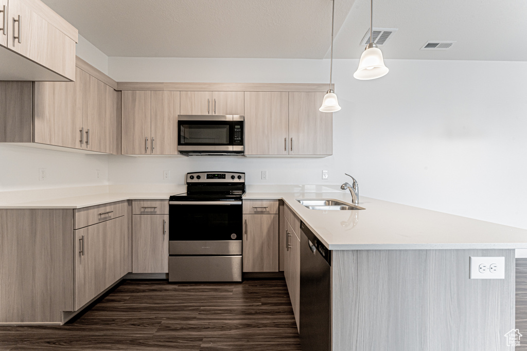 Kitchen with stainless steel appliances, light brown cabinetry, a peninsula, a sink, and light countertops