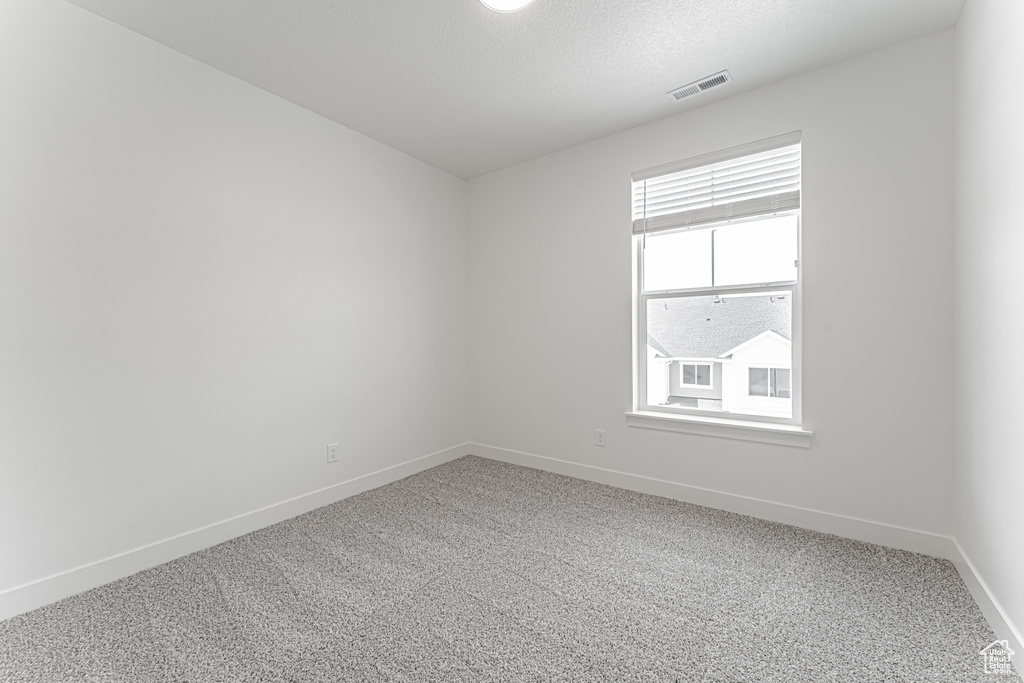 Empty room with light carpet, baseboards, and a textured ceiling