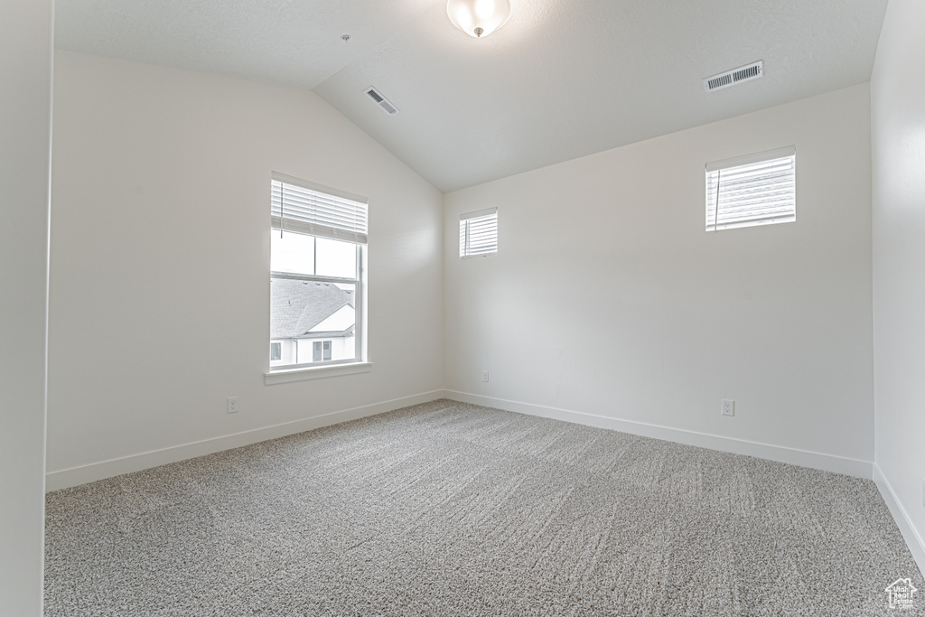 Carpeted spare room with baseboards and vaulted ceiling