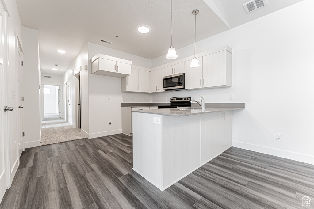 Kitchen with appliances with stainless steel finishes, a peninsula, dark wood-style floors, white cabinets, and recessed lighting