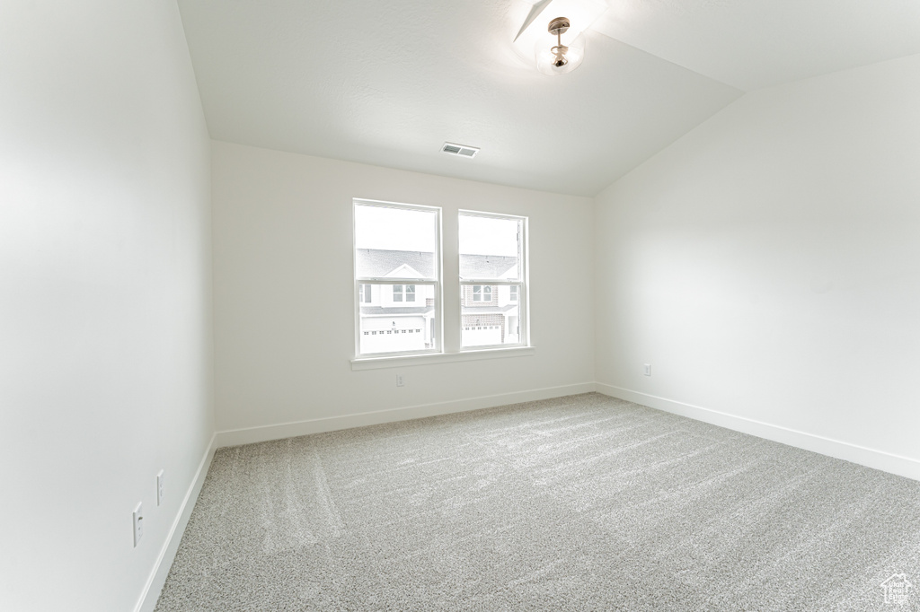 Carpeted empty room featuring baseboards, vaulted ceiling, and visible vents