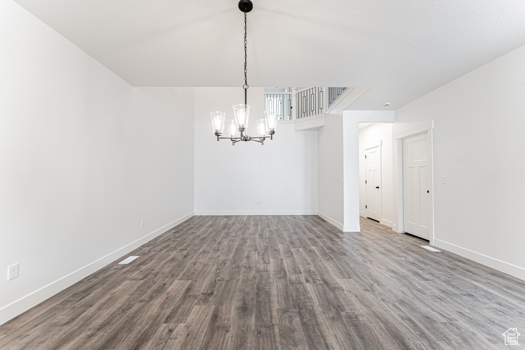 Unfurnished room with dark wood-style flooring, a notable chandelier, and baseboards