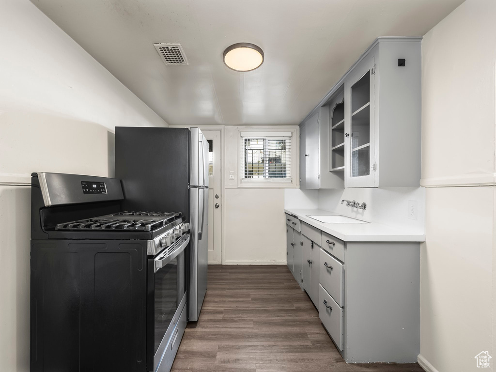 Kitchen with gray cabinets, stainless steel gas stove, dark wood-type flooring, and sink