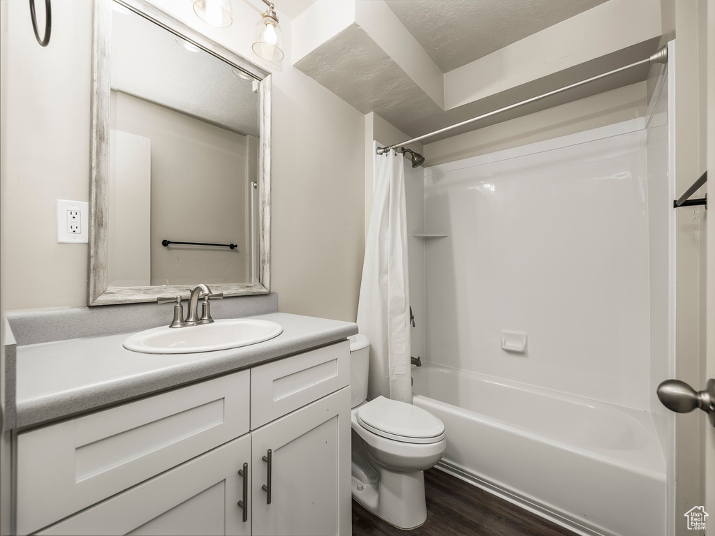 Full bathroom featuring hardwood / wood-style floors, vanity, shower / bath combination with curtain, toilet, and a textured ceiling